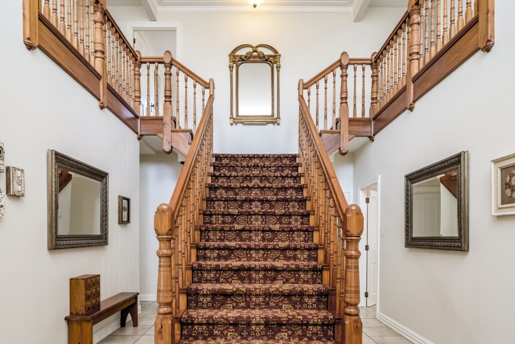 A big wooden staircase with a vintage carpet inside an apartment with white walls